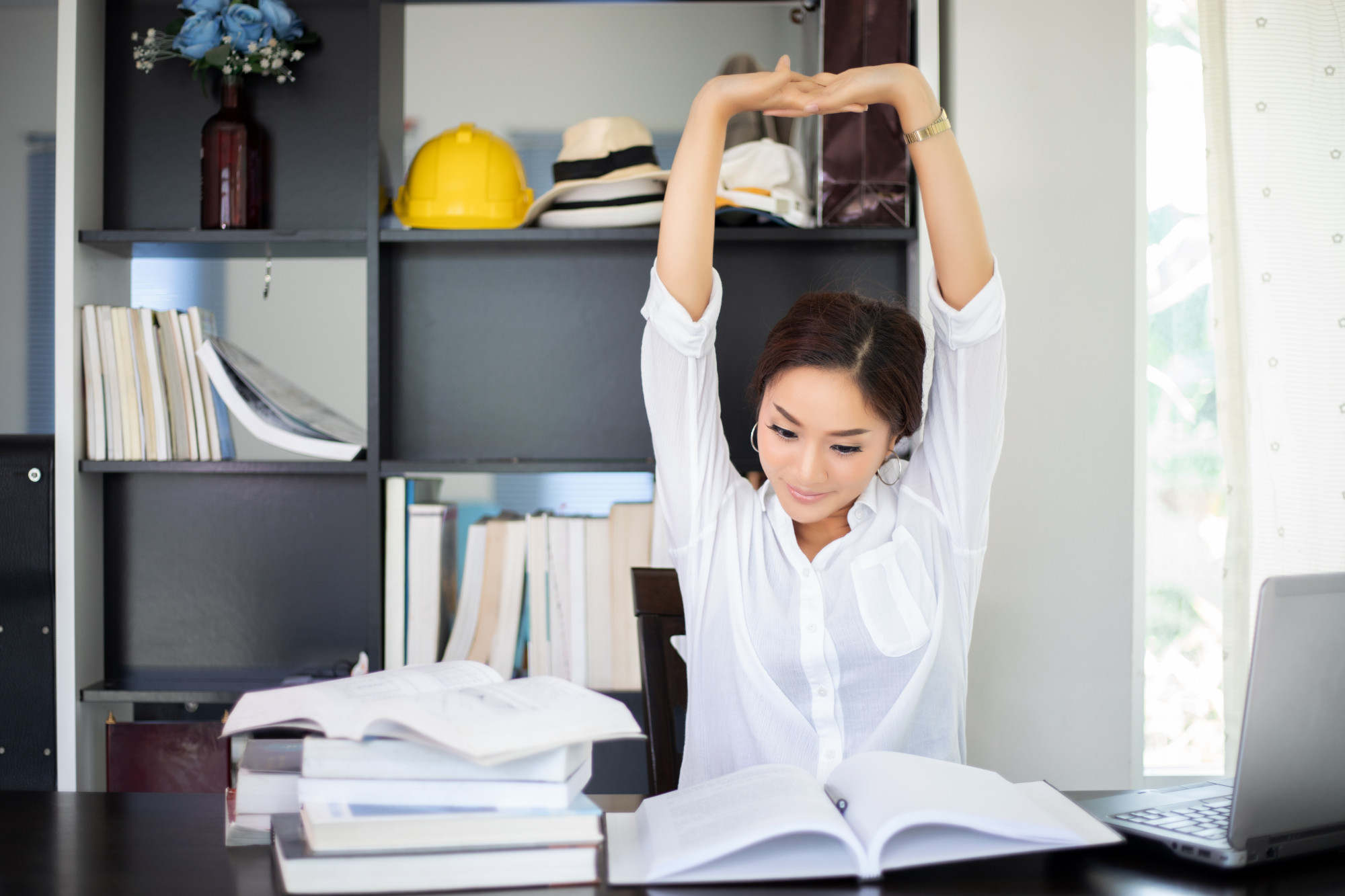 Asian woman stretching after reading book and work hard and smiling in the home office