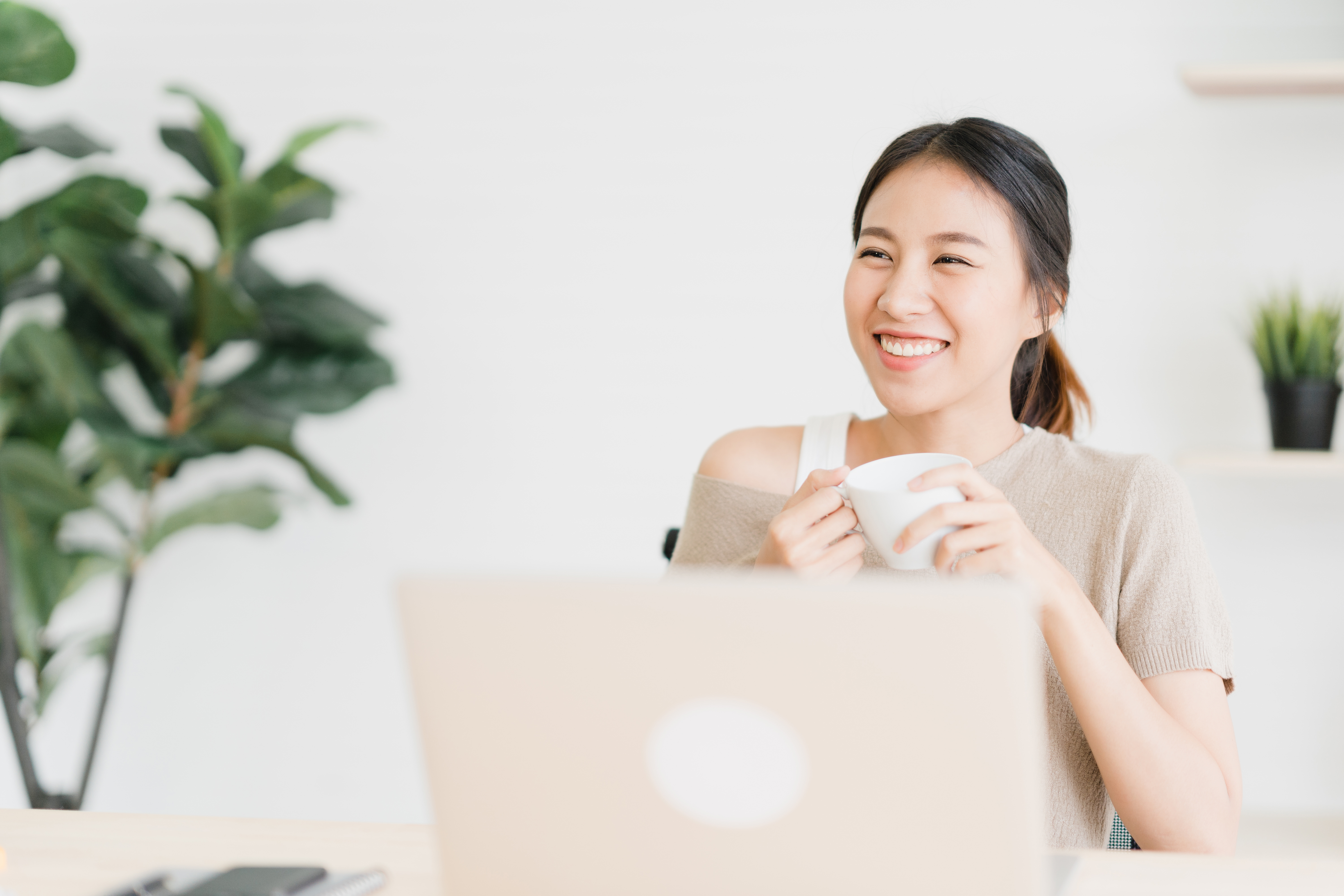 Beautiful young smiling asian woman working on laptop and drinking coffee