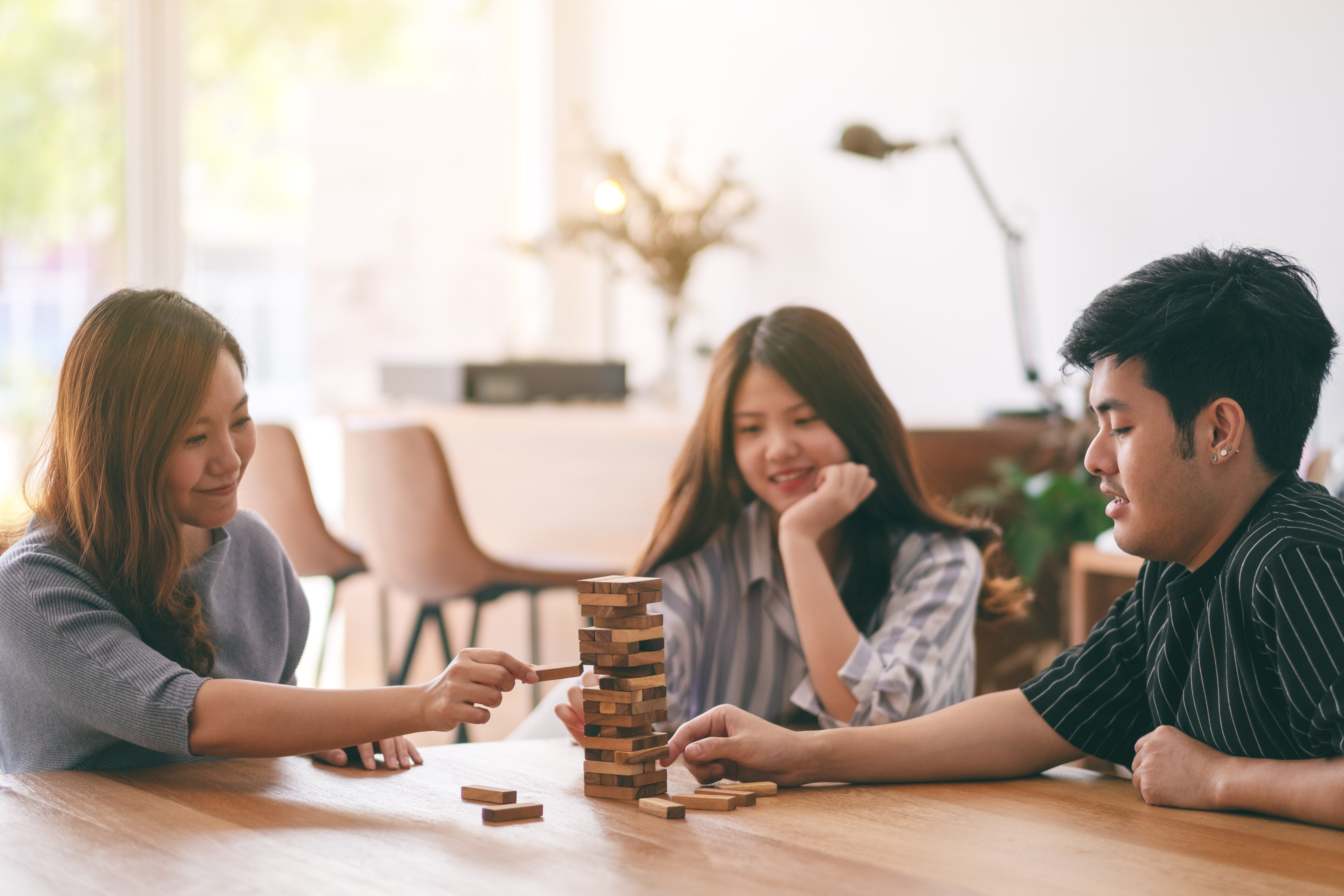 three friends playing jenga together feeling happy doing indoor recreational activities